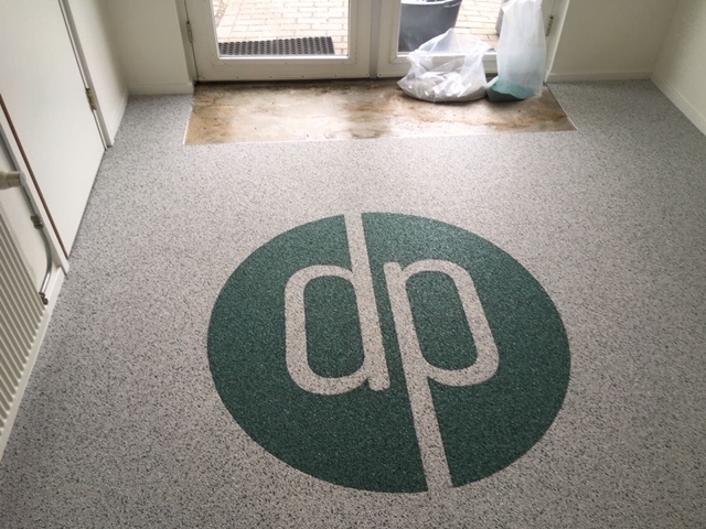 Depoxy-Grindvloeren-grijze-grind-vloer-met-groen-logo-initialen-bedrijf-verwerkt-in-grind-vloer